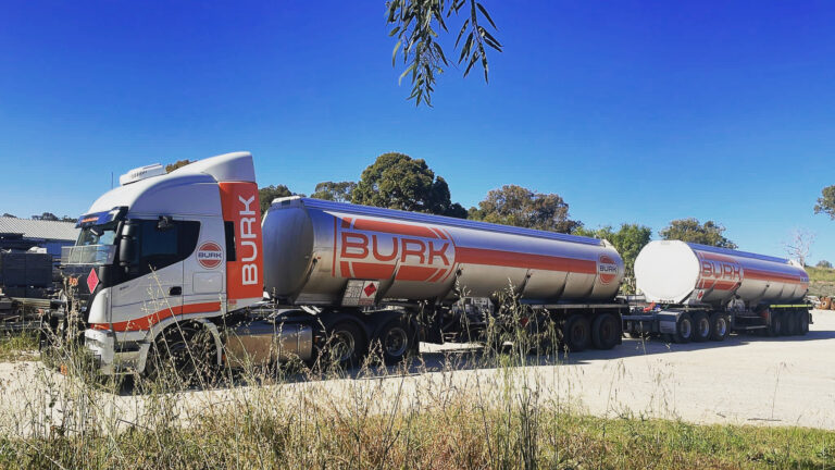 Burk Fuel road train with triple tanker trailers parked on a rural site under clear blue sky.