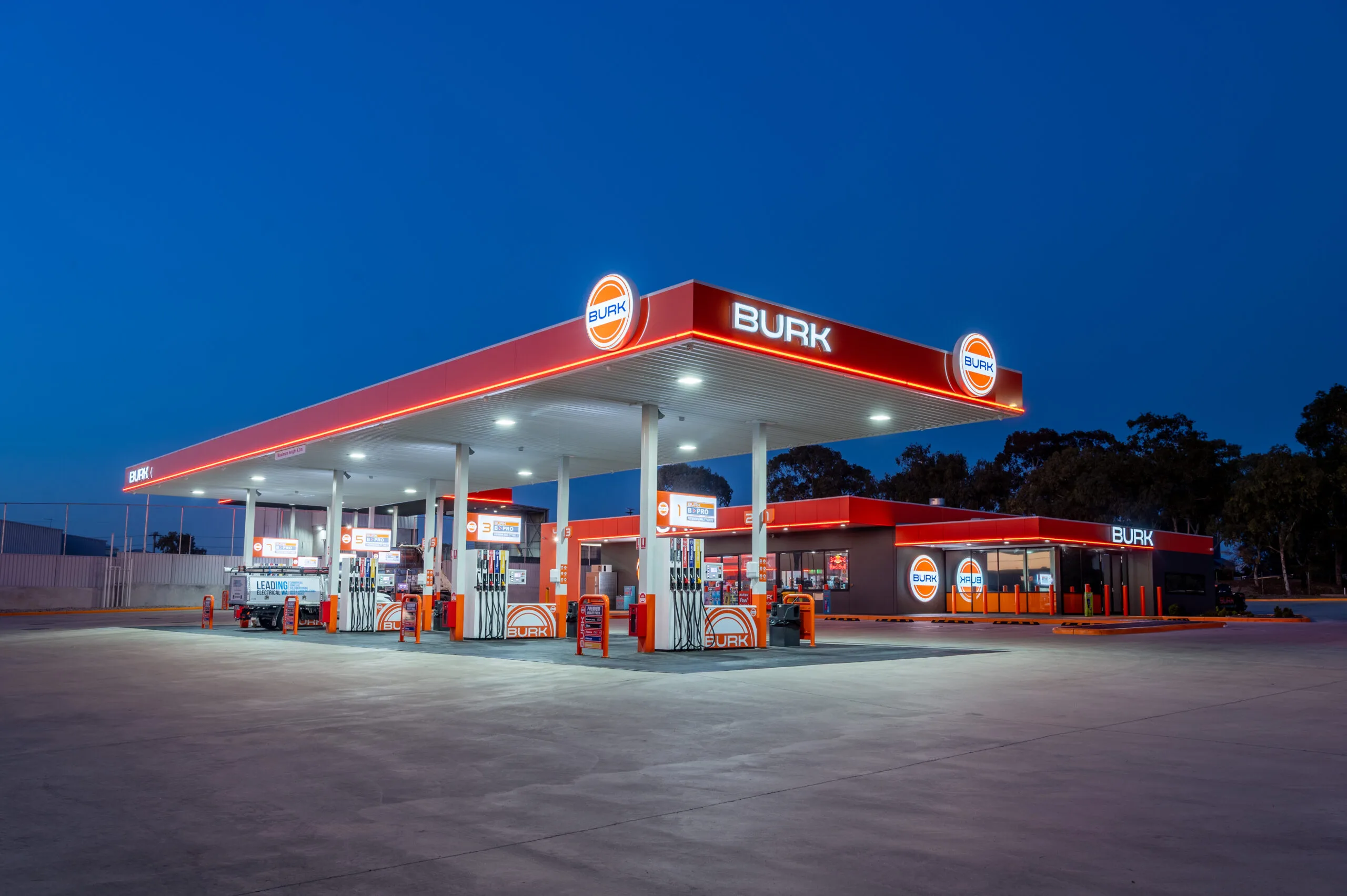 A gas station glowing at night, showcasing a lit sign that says "Burk Fuel Pump."