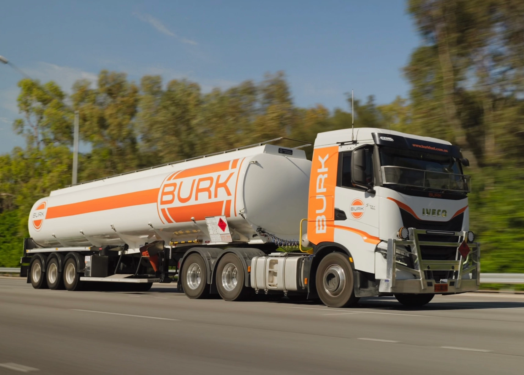 A large Burk Fuel tanker truck driving down the road, transporting fuel through a rural landscape.